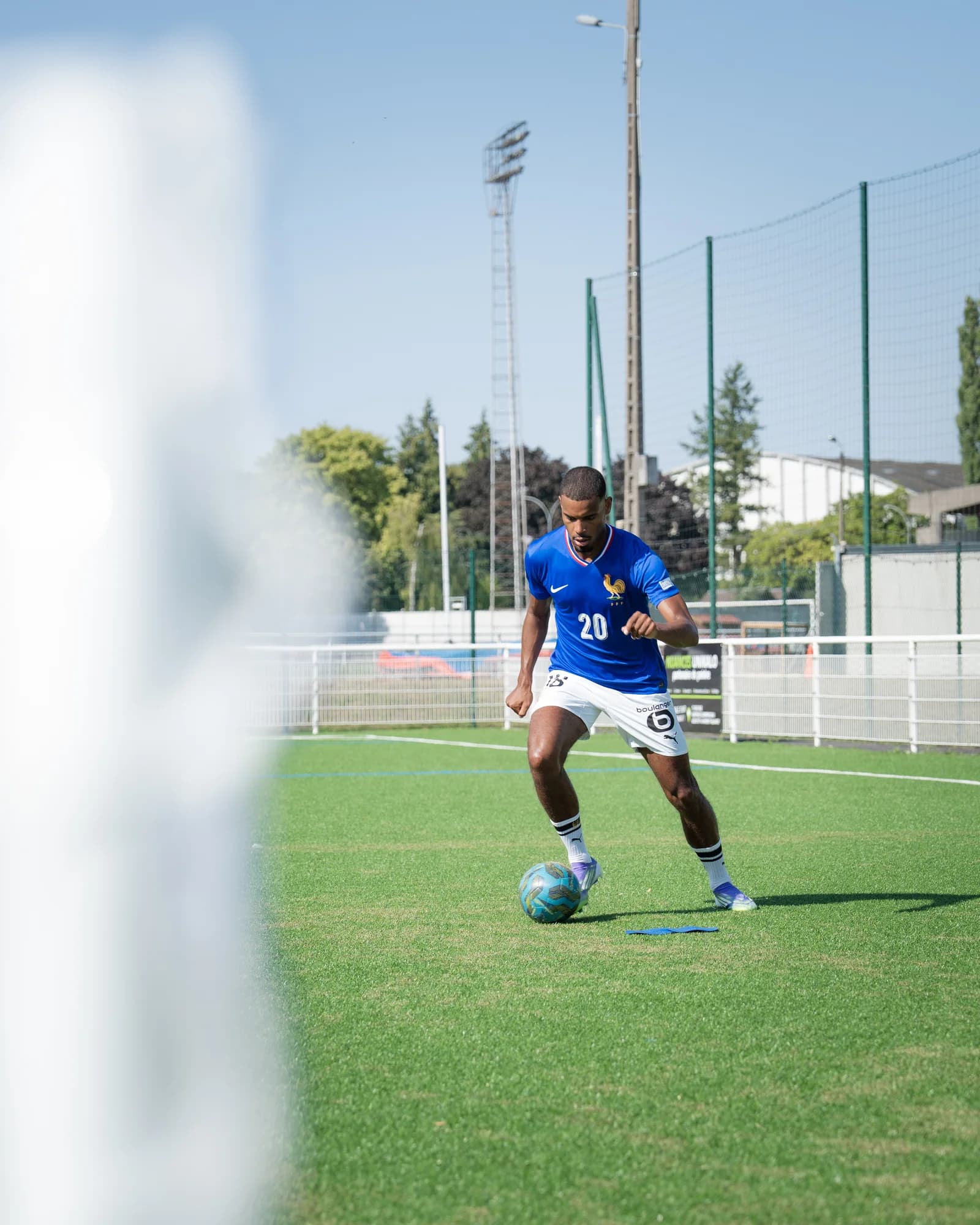 Andy Diouf in the blue France number 20 shirt dribbling under a clear summer sky, framed through the goalpost.