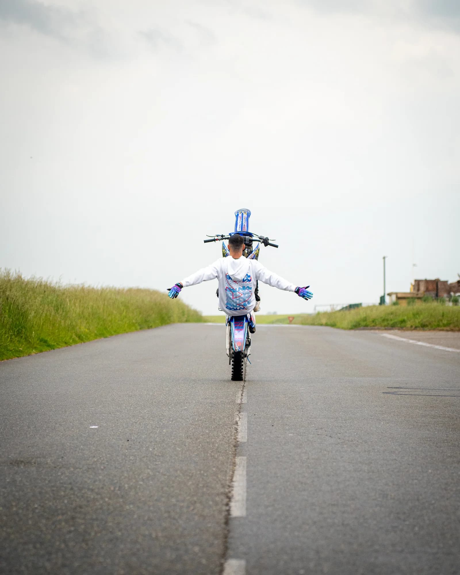 Arms outstretched in total control, the rider balances a wheelie along the centre line of an empty road.