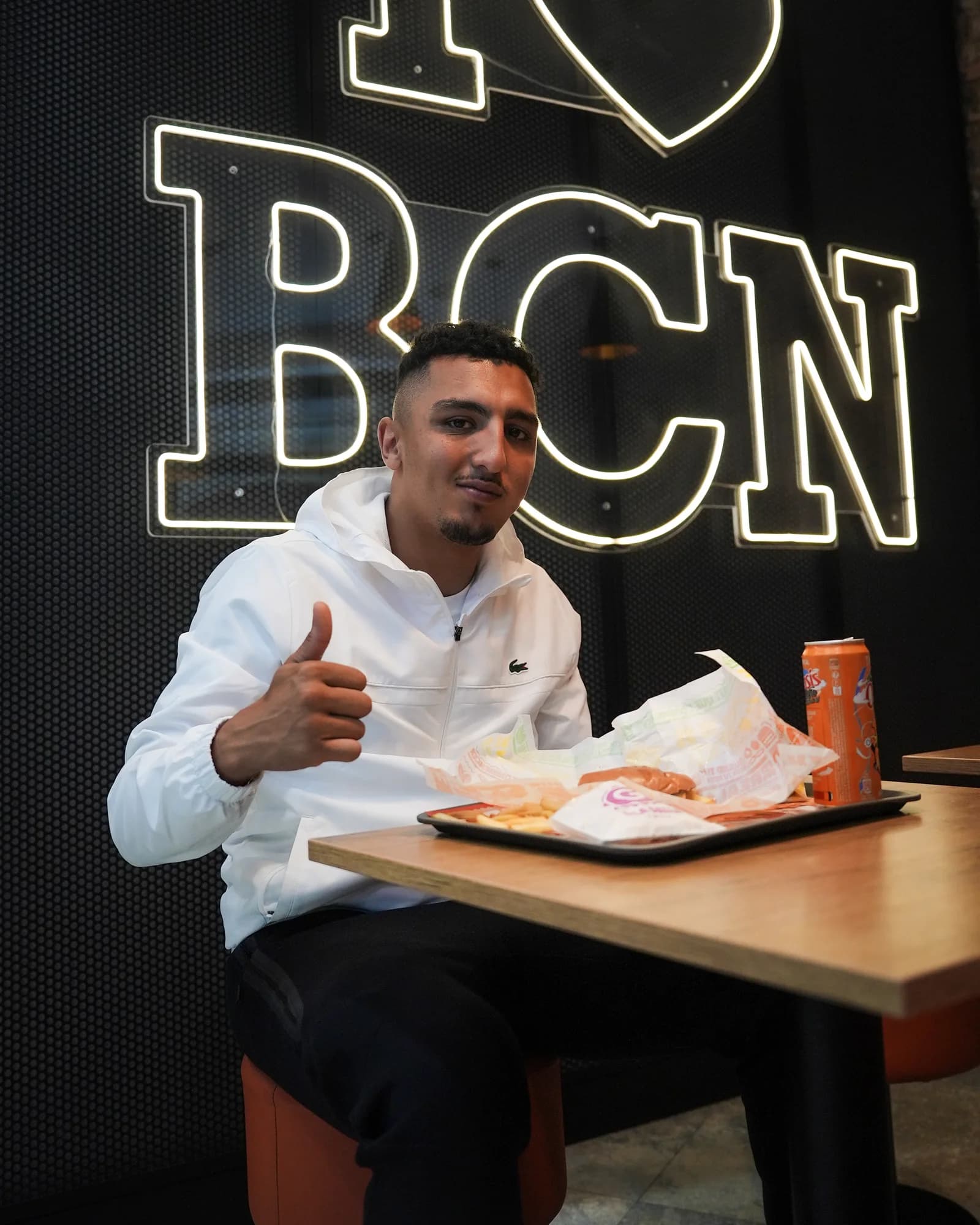 Morad gives a thumbs-up over his tray, framed by the illuminated BCN letters.