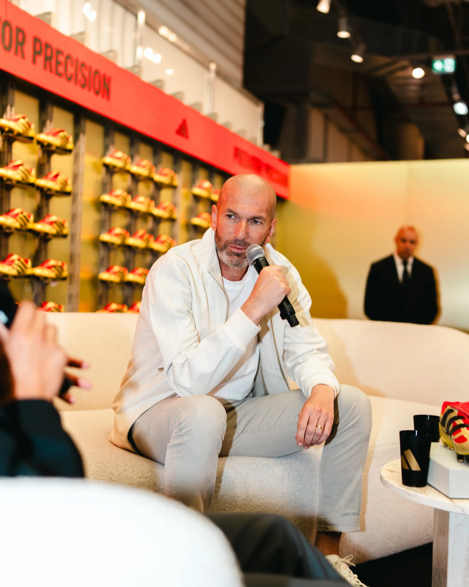 Zidane holds court on a cream sofa, framed by a wall of gold Predator boots.