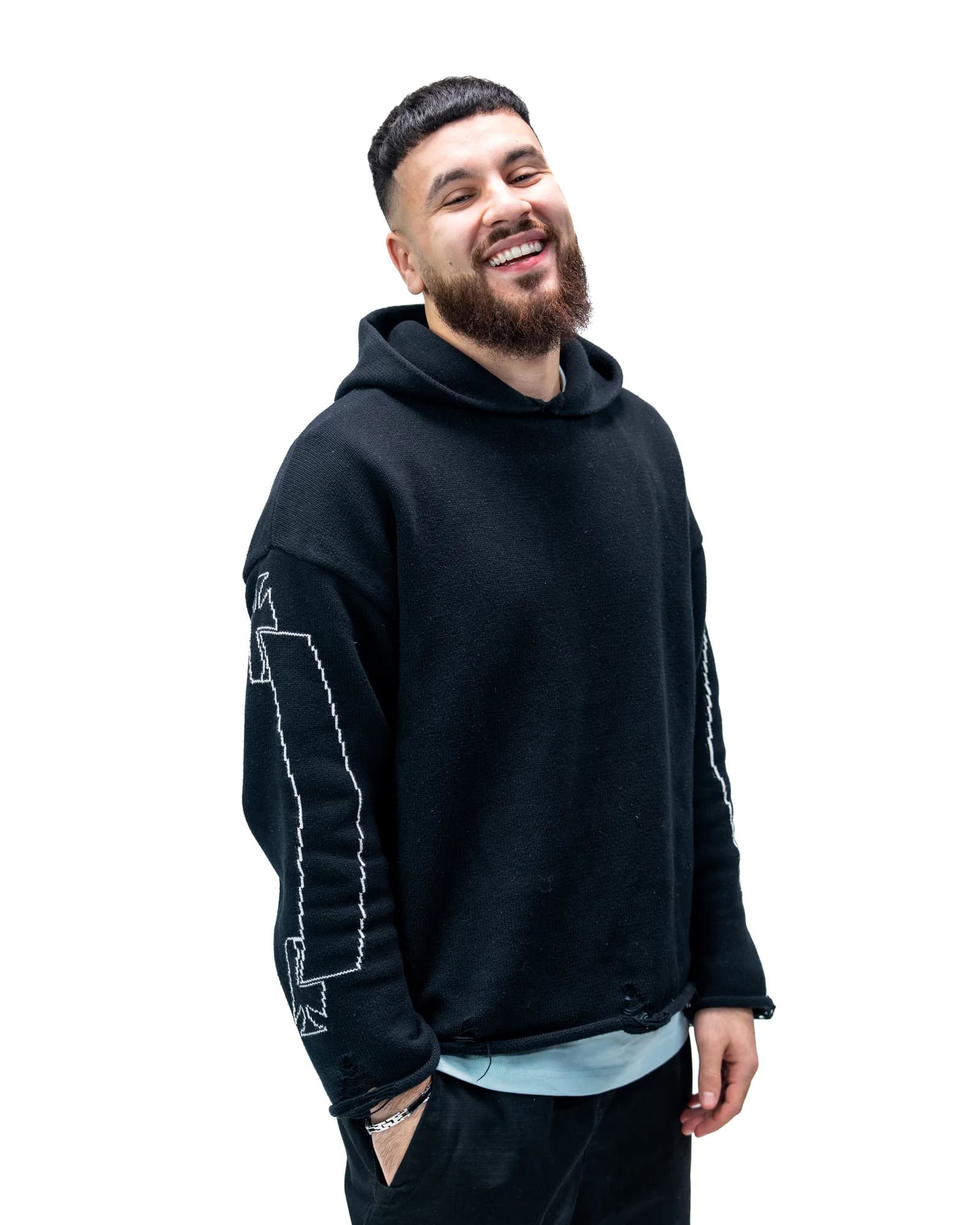 Fukay laughing warmly in a black knit hoodie, hand in pocket against a clean white backdrop.